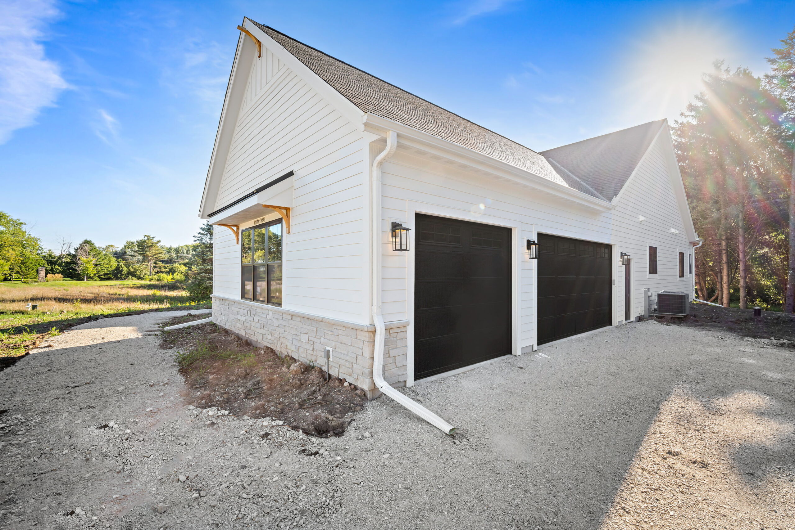 Side exterior of home with two-car garage, white siding, stone base, and black garage doors