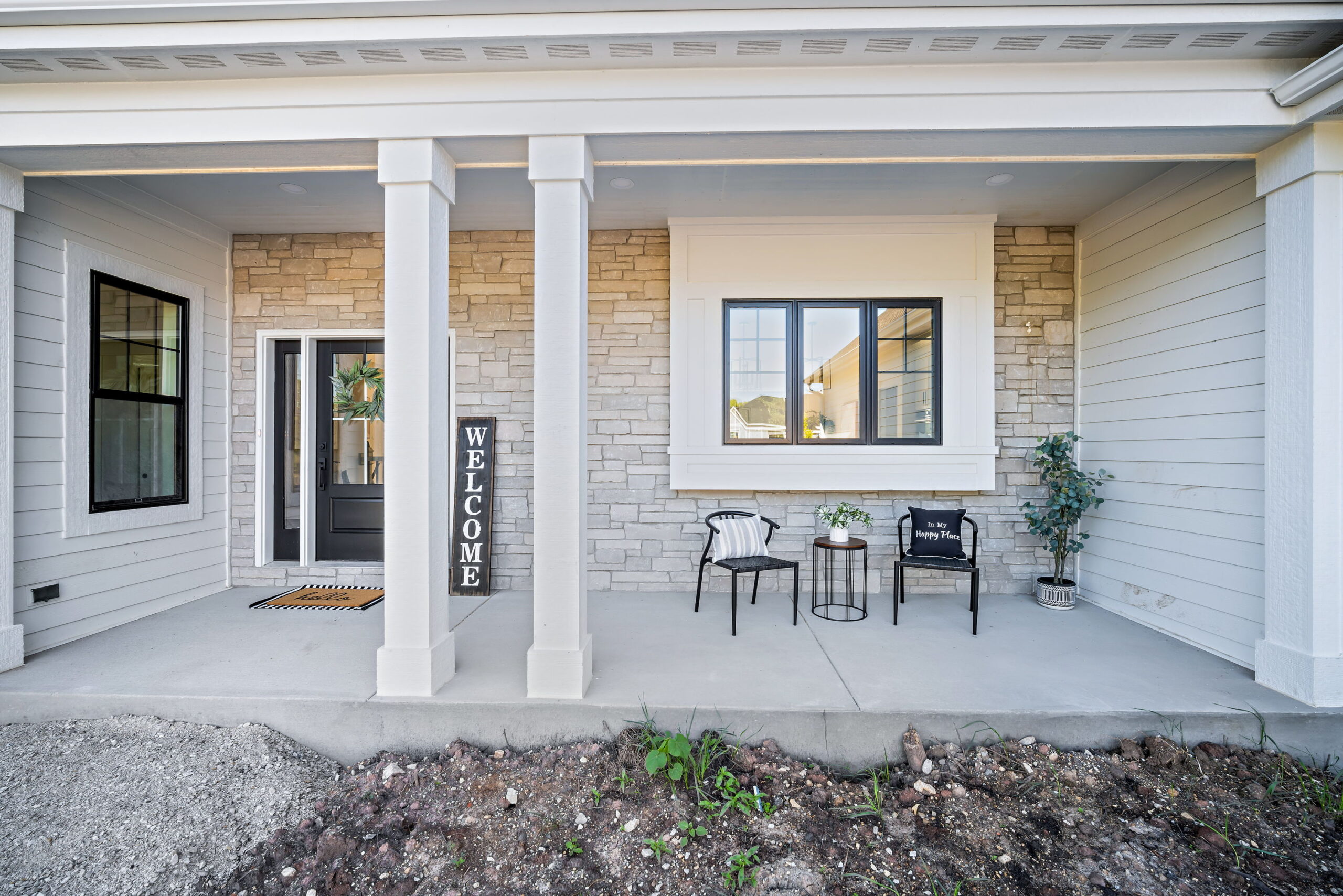 Covered front porch with stone exterior, white columns, and seating area at custom built home