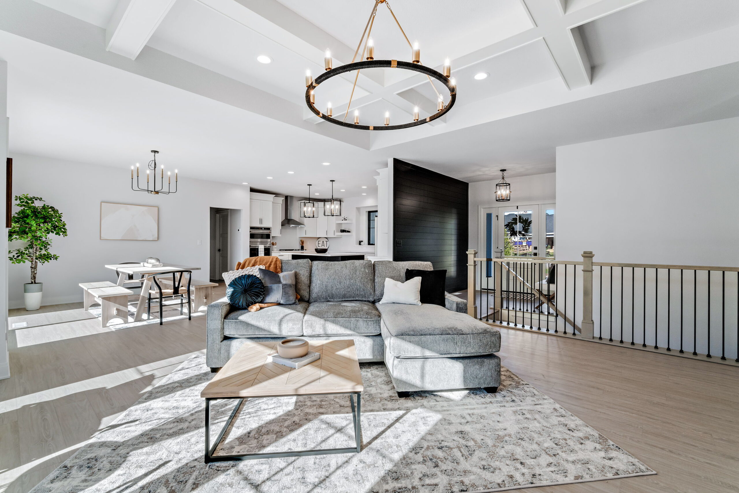 Open concept living room with sectional sofa, coffered ceiling, chandelier, and staircase railing