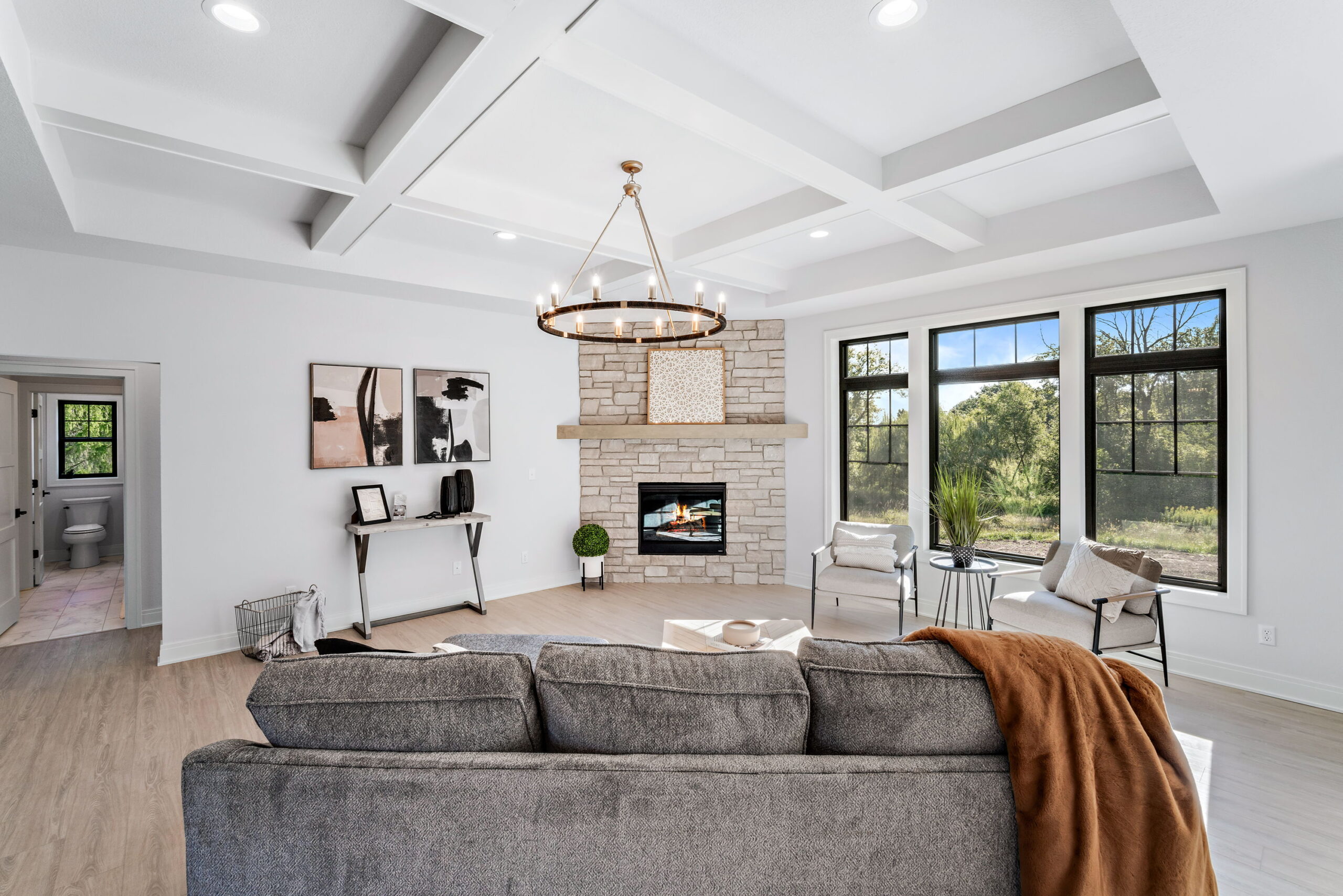 Living room with stone fireplace, coffered ceiling, large windows, and modern seating area