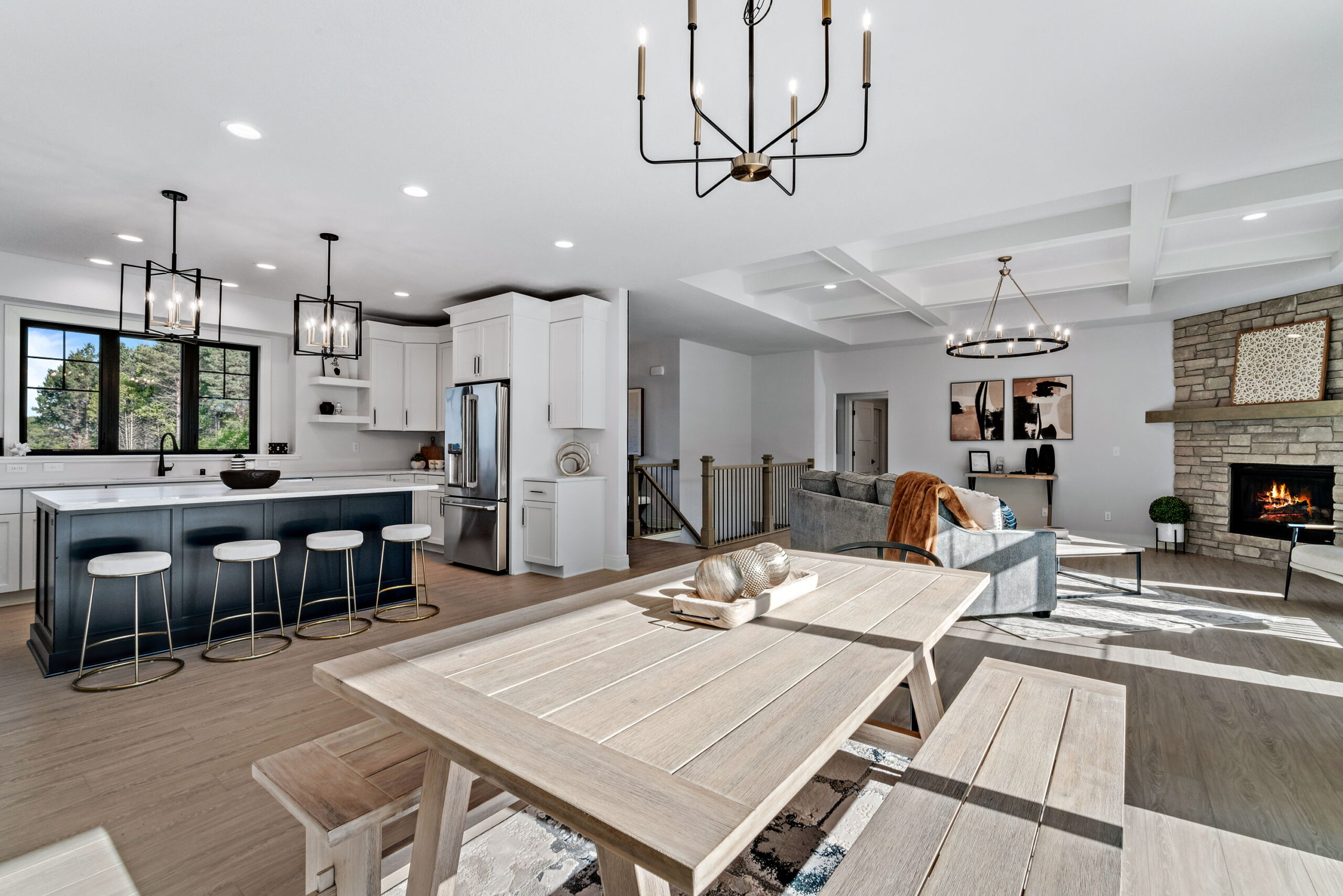 Open concept kitchen, dining, and living area with large island, coffered ceiling, and stone fireplace