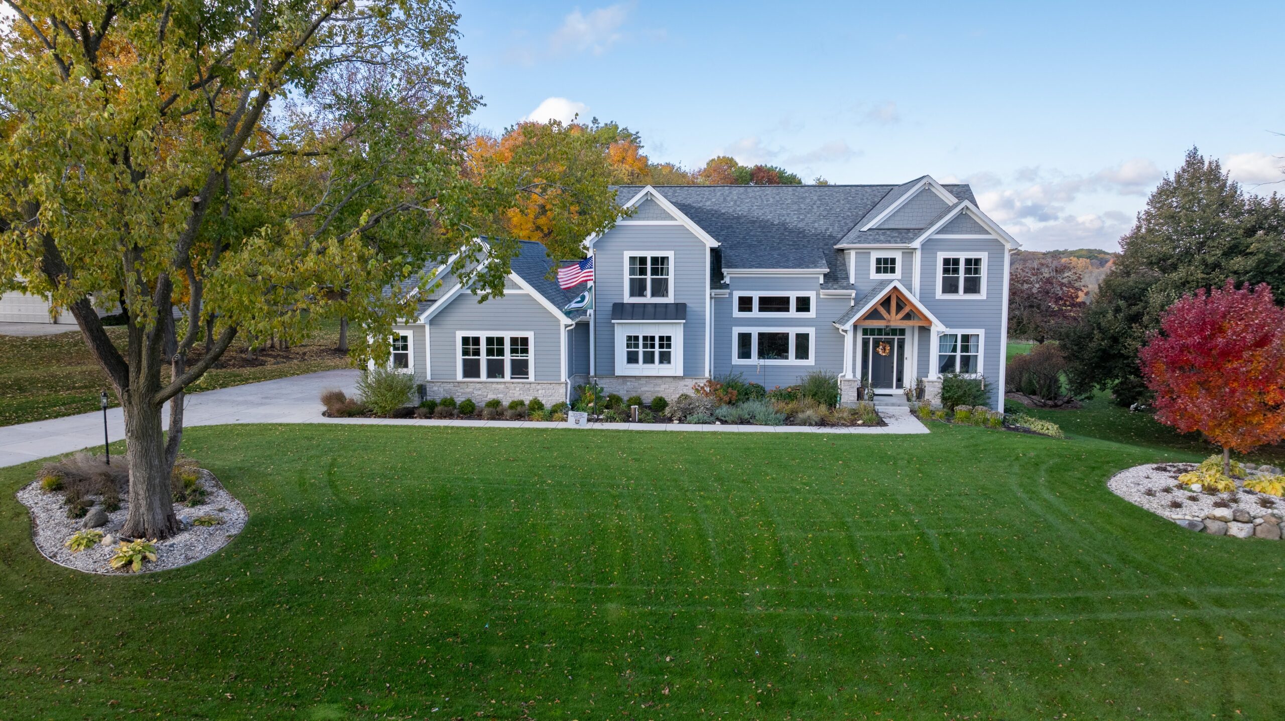 custom home front exterior with large green lawn, landscaping, and gray siding