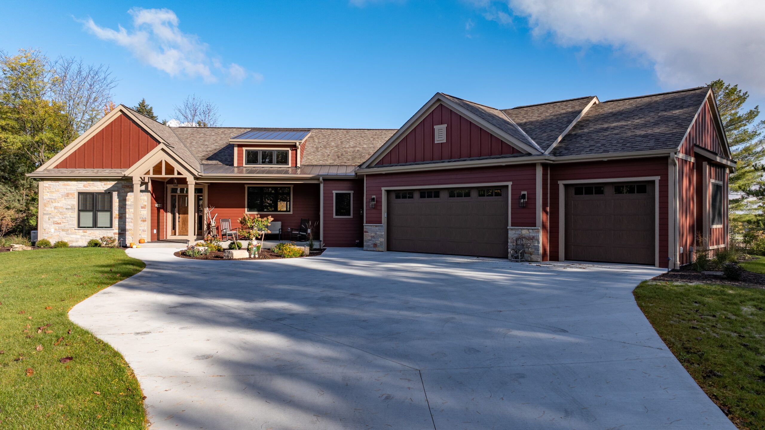 custom home exterior with red siding, stone accents, and three car garage with curved driveway