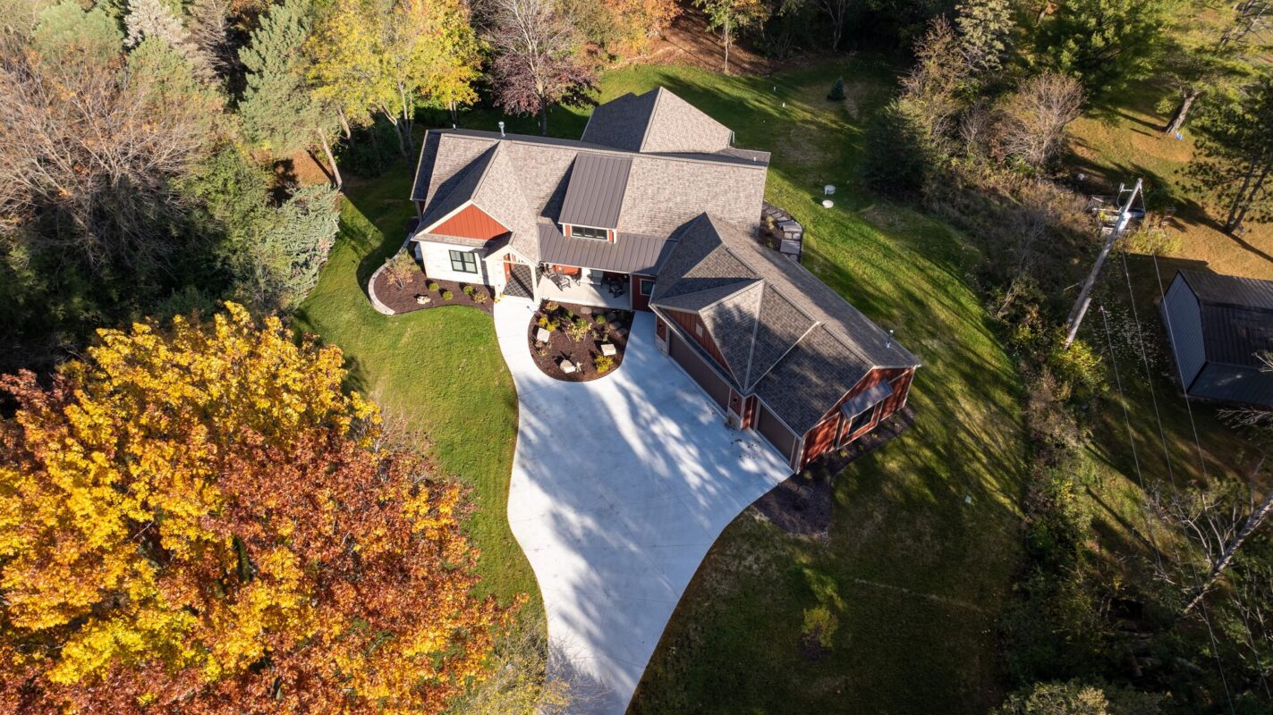 aerial view of custom home with curved driveway, fall trees, and landscaped yard