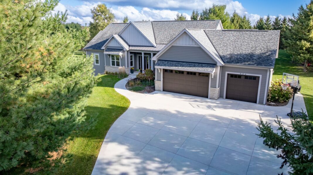 custom home exterior with gray siding, curved driveway, and three car garage