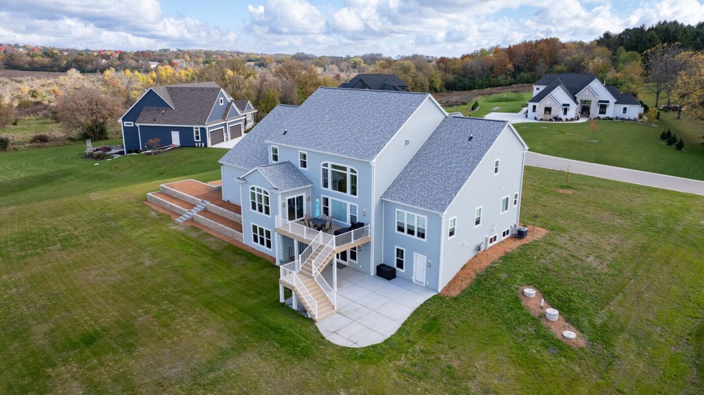 aerial view of custom home rear exterior with elevated deck, stairs, and walkout patio