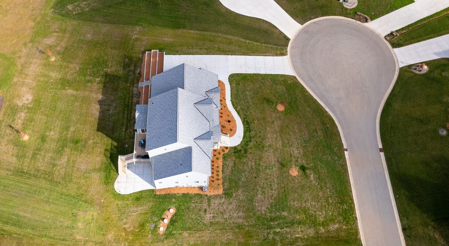 aerial view of custom home on large lot near cul-de-sac with driveway and landscaping
