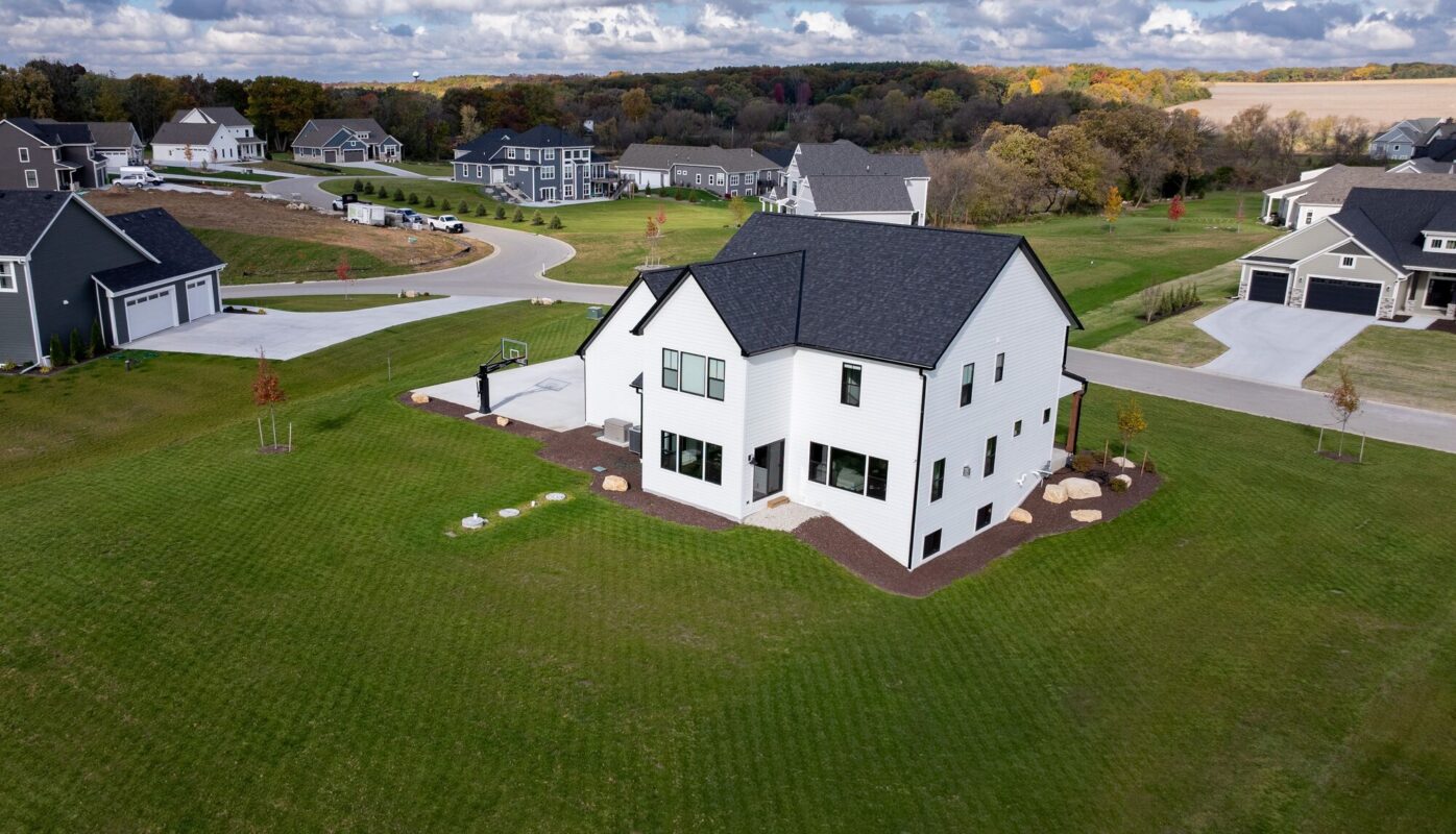 aerial view of custom home with white exterior, large yard, and surrounding neighborhood