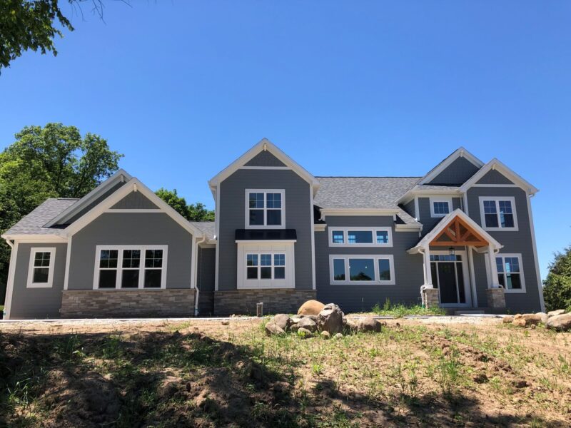 custom home exterior with gray siding, gabled rooflines, and covered front entry