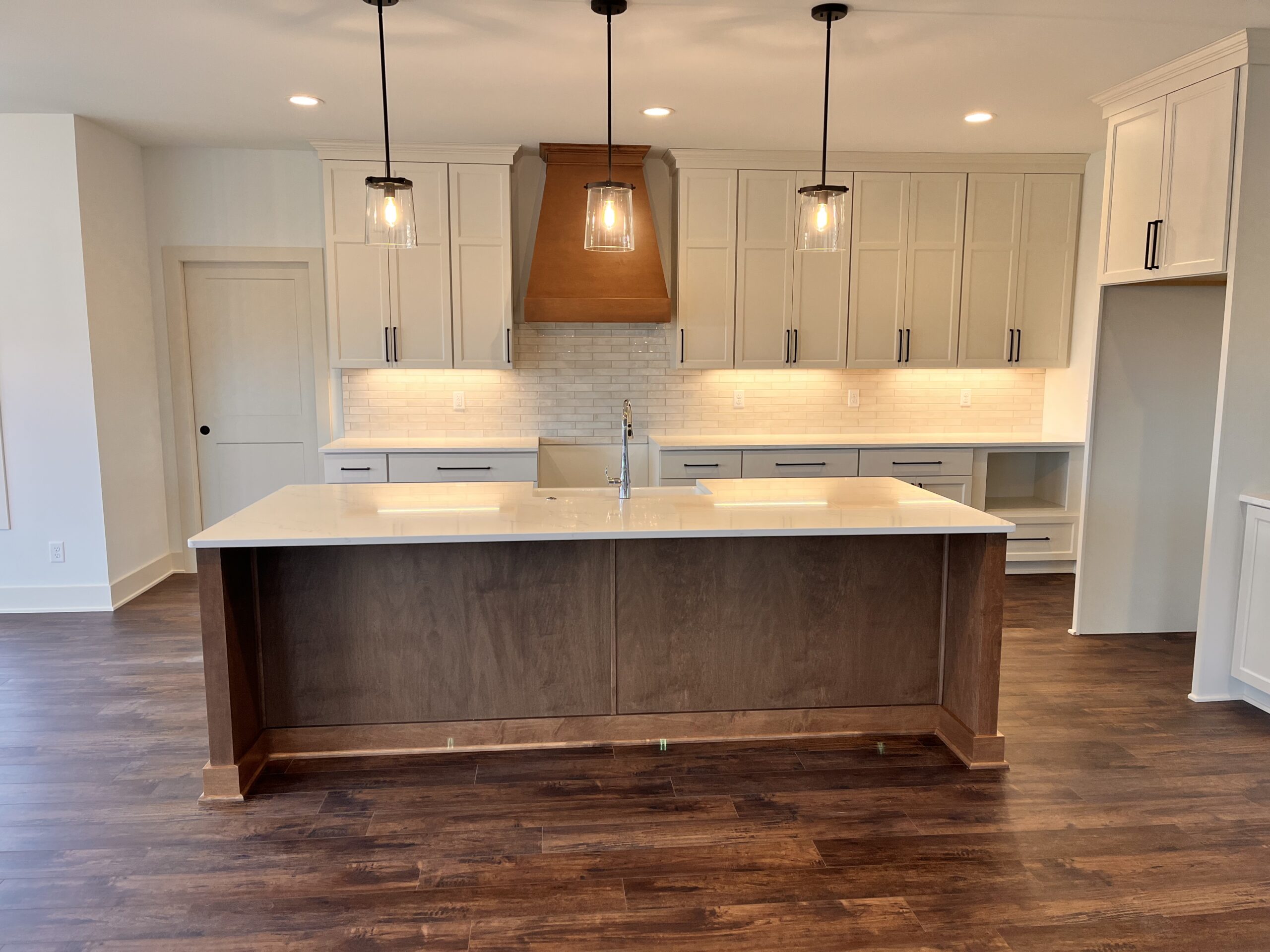 Yaun Home kitchen with large wood island, white cabinetry, quartz countertops, and custom wood range hood