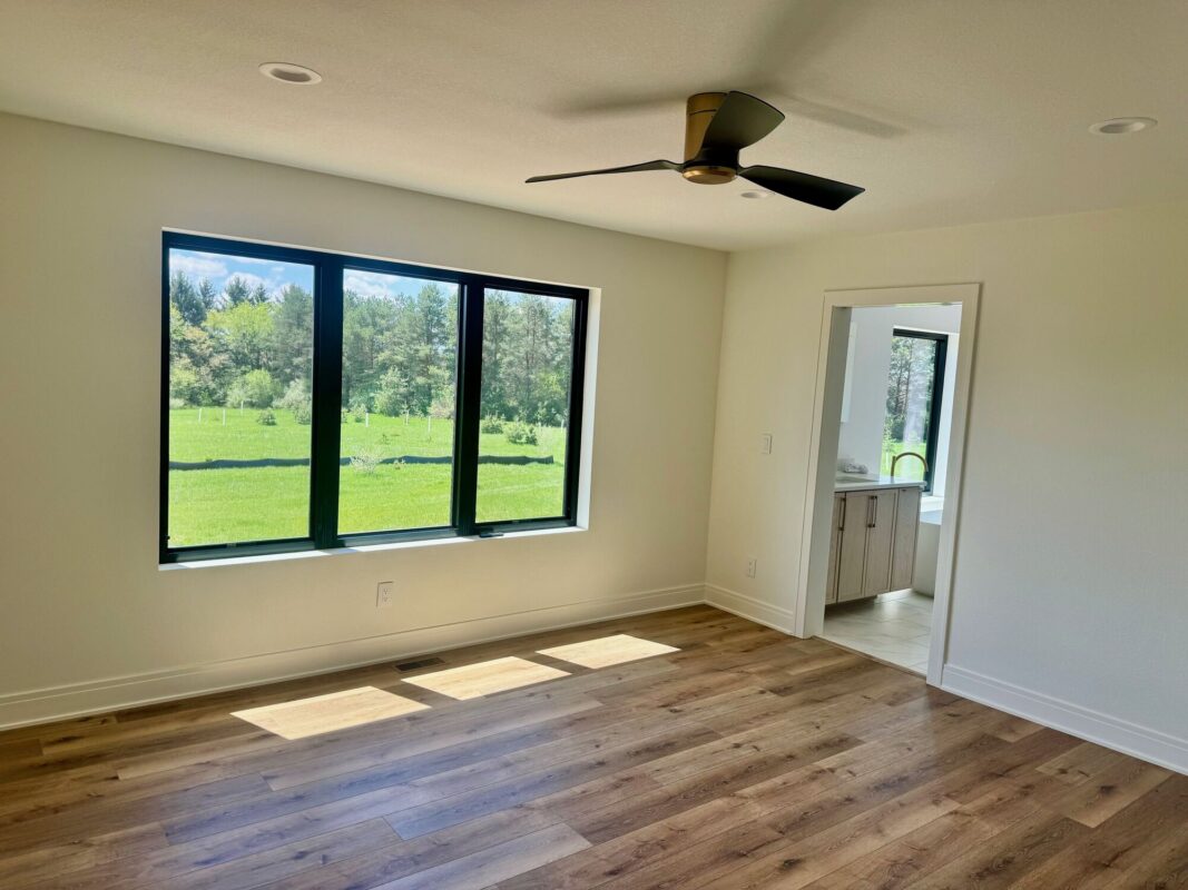 custom home primary bedroom with large window, wood flooring, and modern ceiling fan