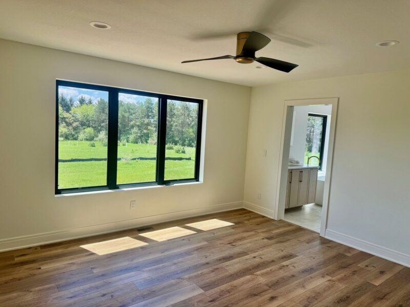 custom home primary bedroom with large window, wood flooring, and modern ceiling fan