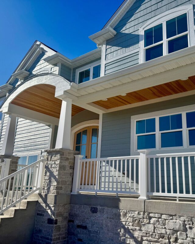 Morrow Home front porch with stone columns, white railing, wood soffit ceiling, and gray siding