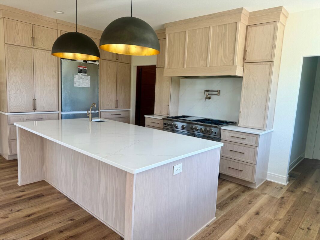 custom home kitchen with large island, light wood cabinets, and modern pendant lighting